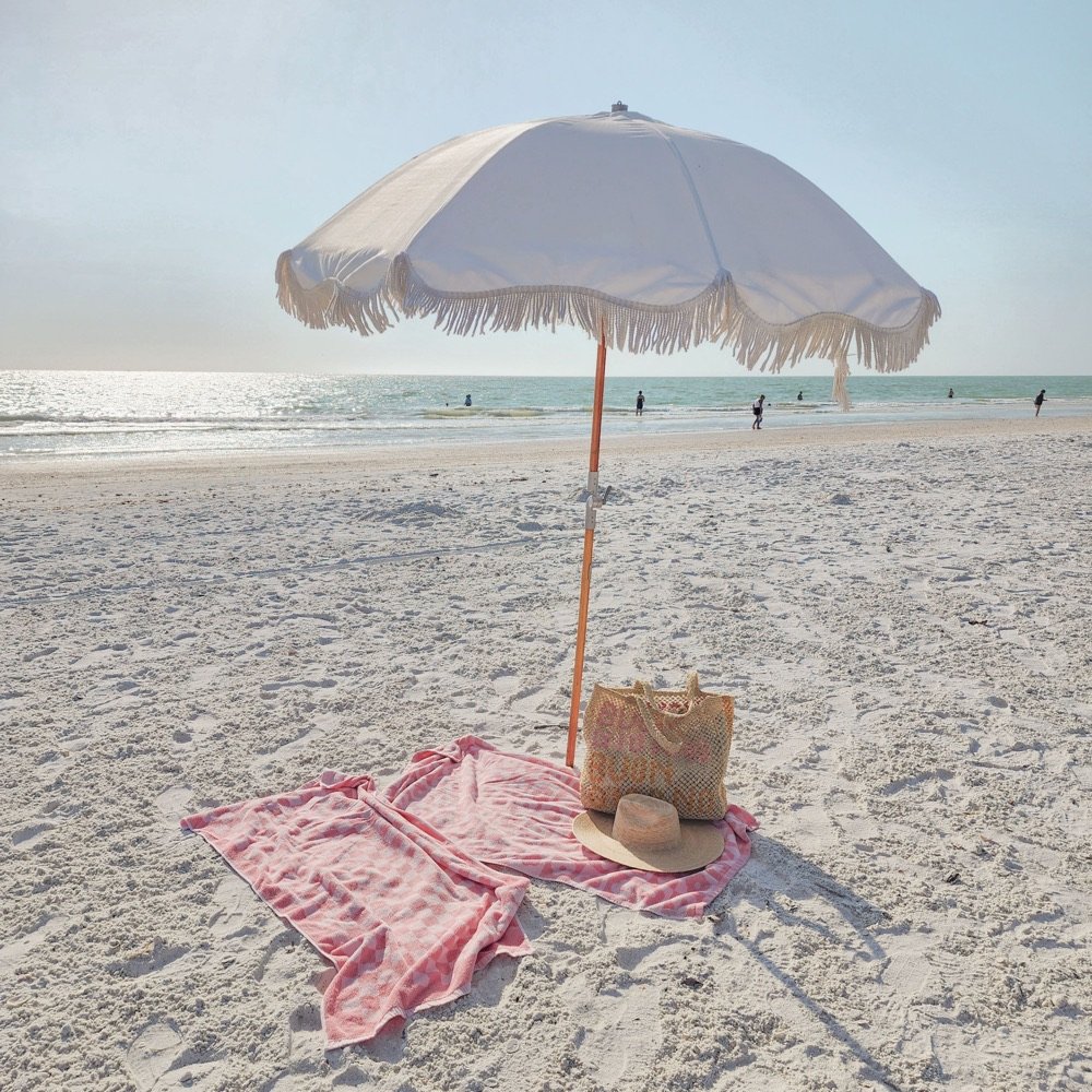 White fringed beach umbrella and towel on the sand