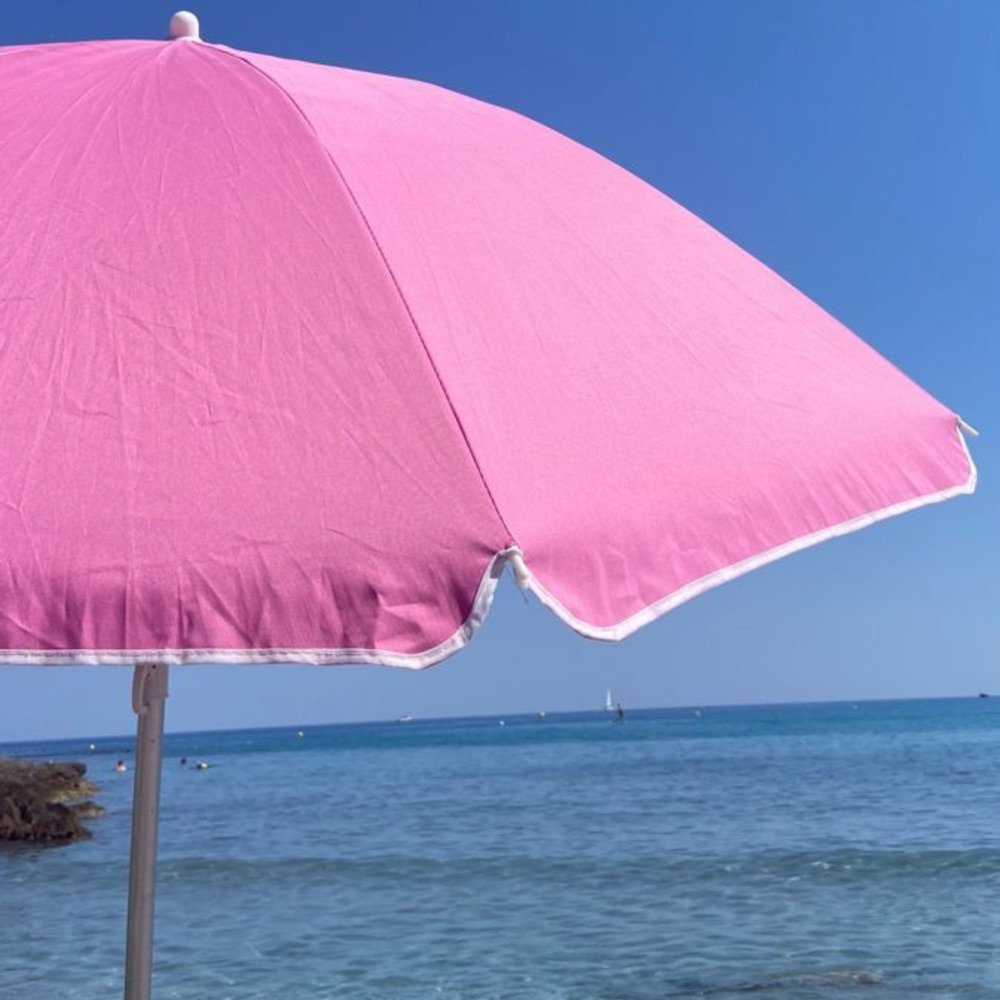 Pink beach umbrella against a blue sky and sea