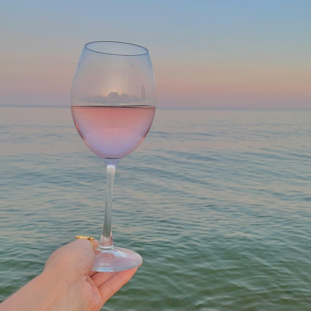 Glass of rosé held up to a calm pink sea