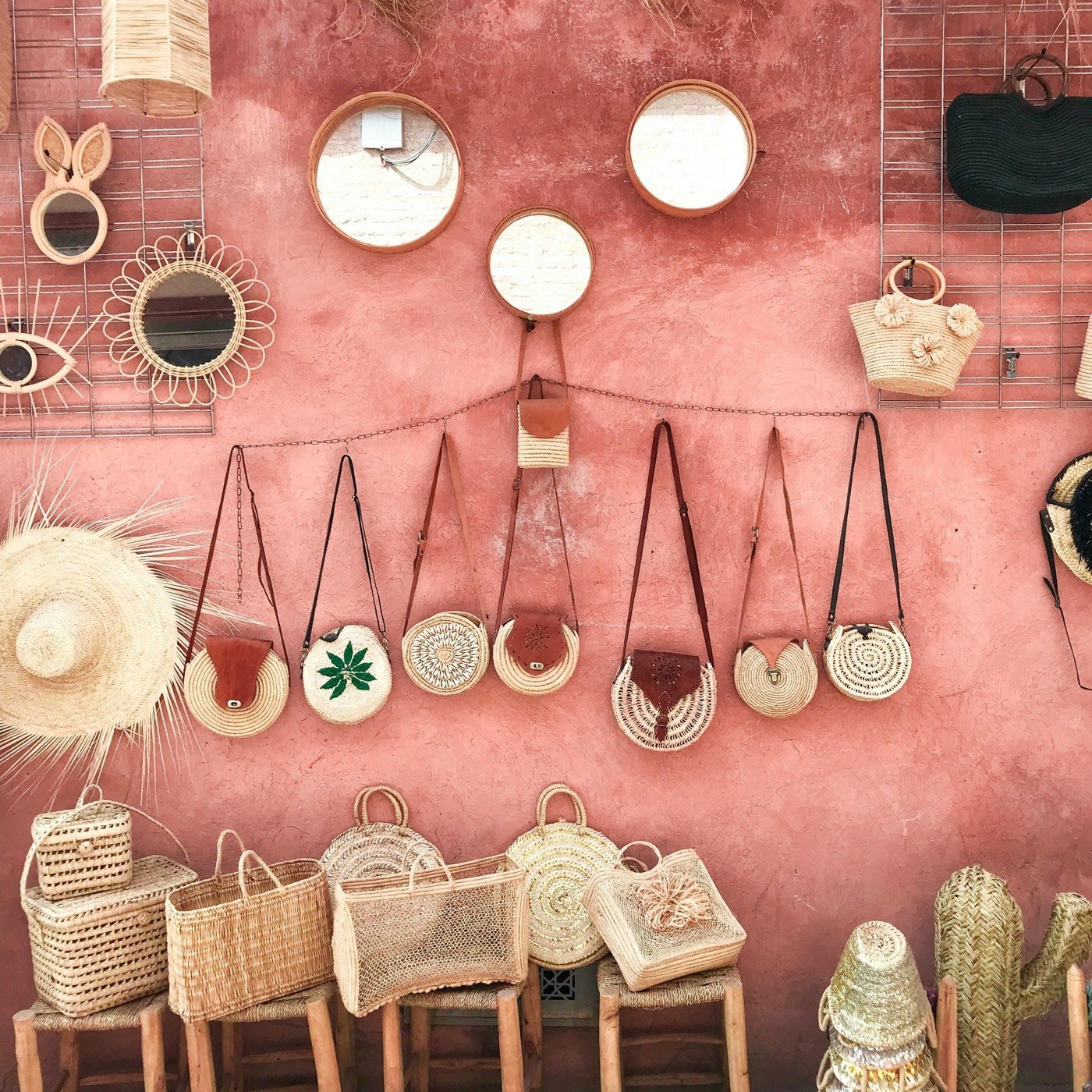 Woven bags, straw hats and mirrors hanging on a pink market wall